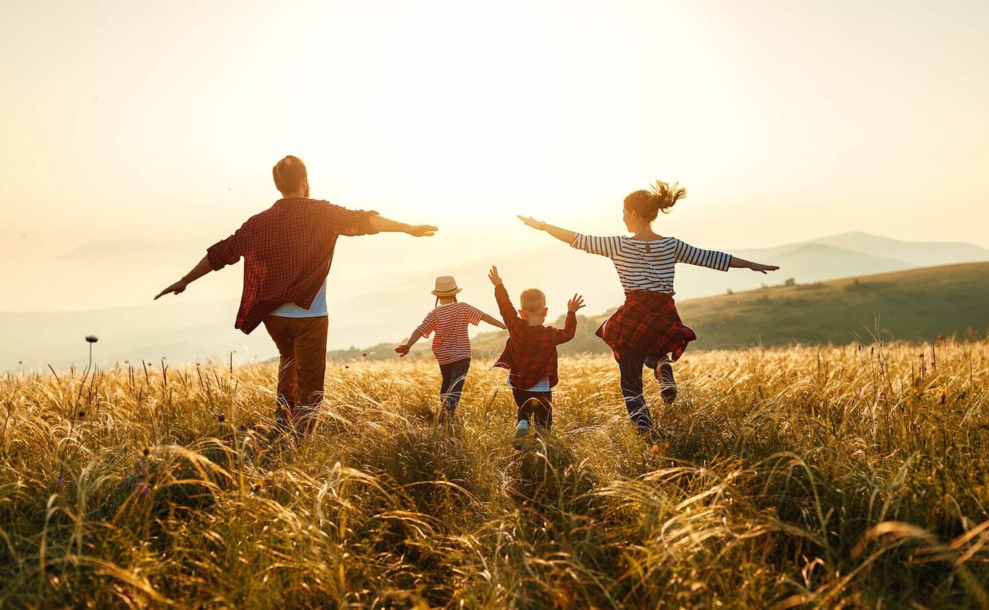 A young family running through a field at sunset