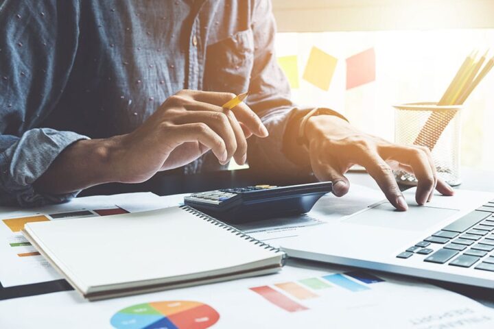 A pair of hand using a calculator as well as a laptop and a notebook