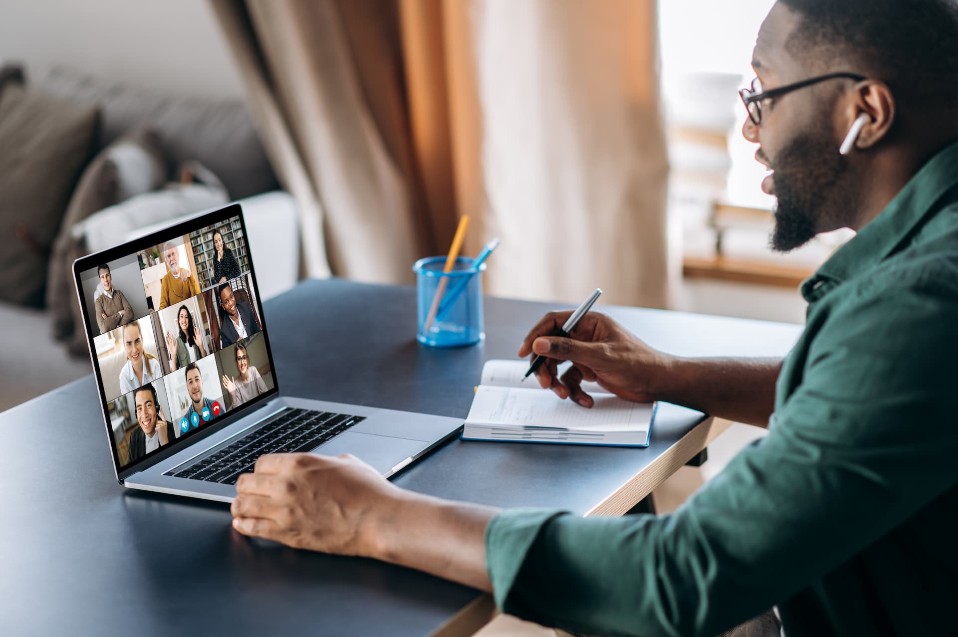 A man on a group video call webinar on his laptop while taking notes on some paper
