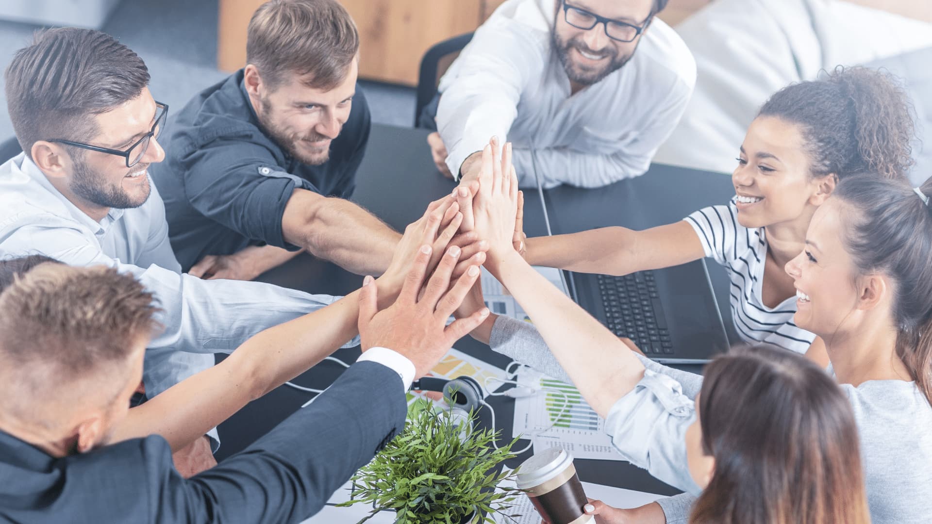 A group of teammates sitting around a desk performing a group high five