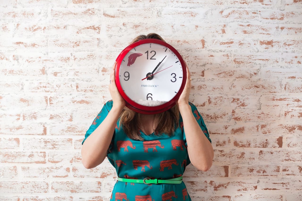 A woman holding a clock in front of her face