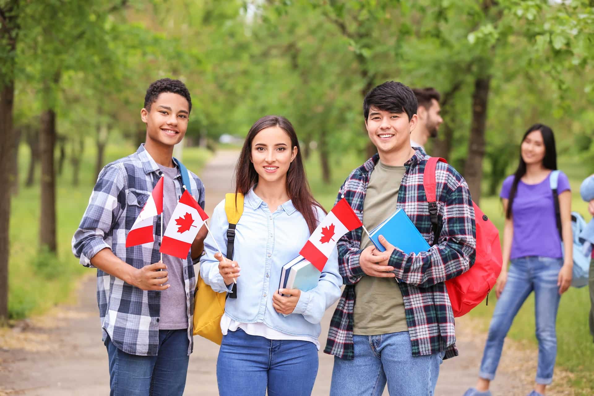Three Canadian students holding books and miniature Canadian flags