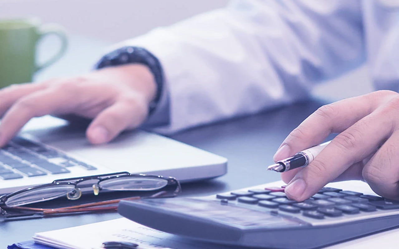 A doctor in a lab coat using a calculator and a laptop