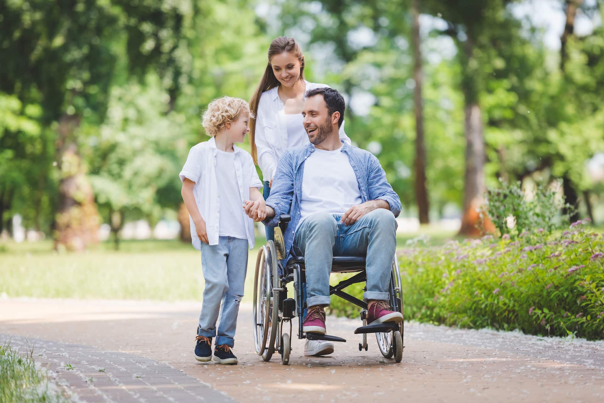 A man in a wheelchair being pushed by his wife while he talks to his child