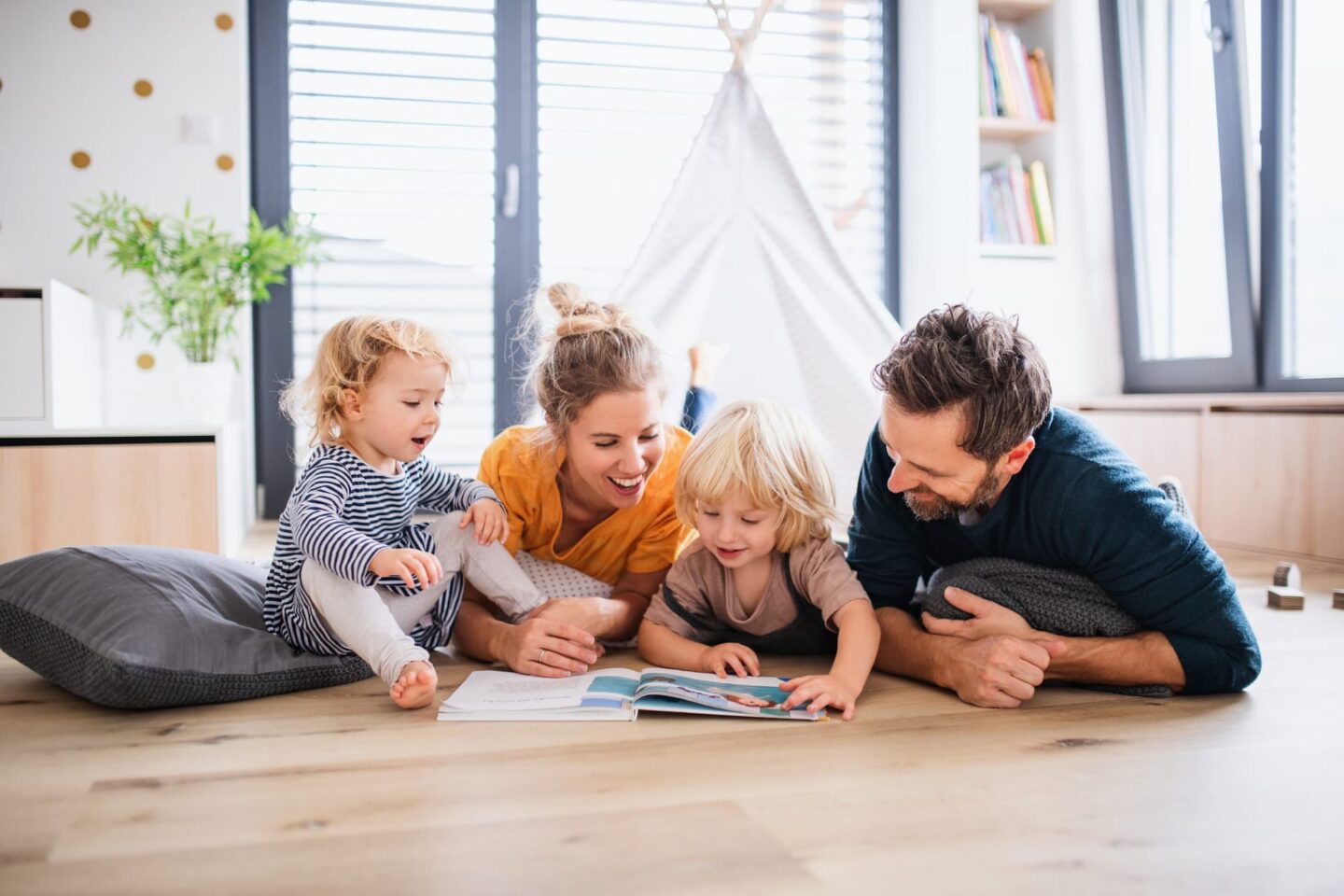 A young family laying on the floor together reading a magazine