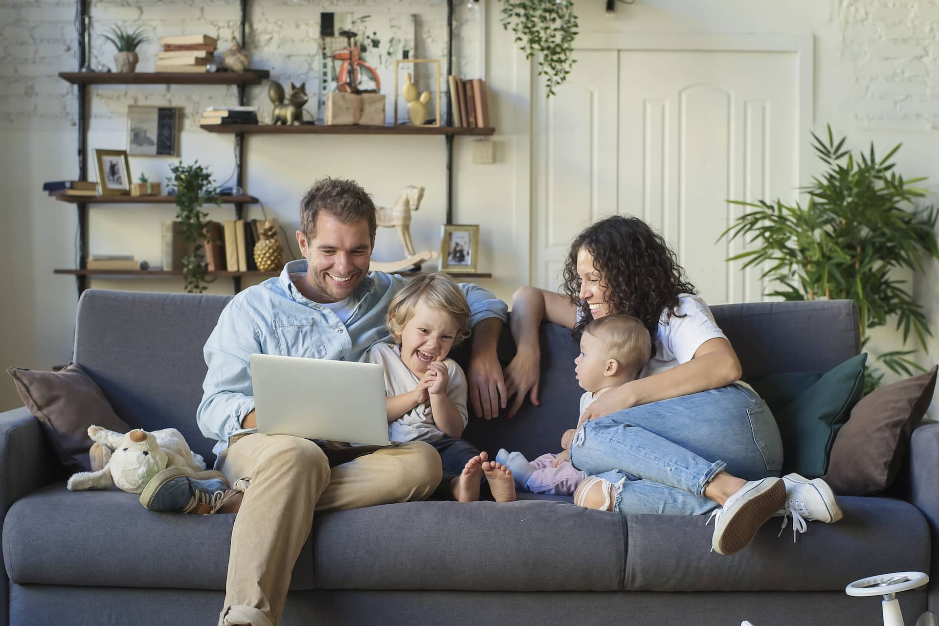 Young family sitting on couch goofing around while the dad is looking at a laptop