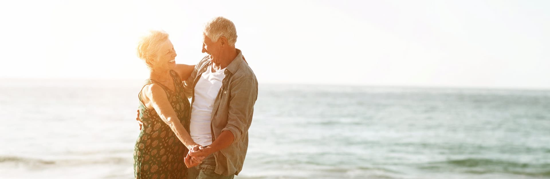 Two retirees dancing on a beach during a sunset