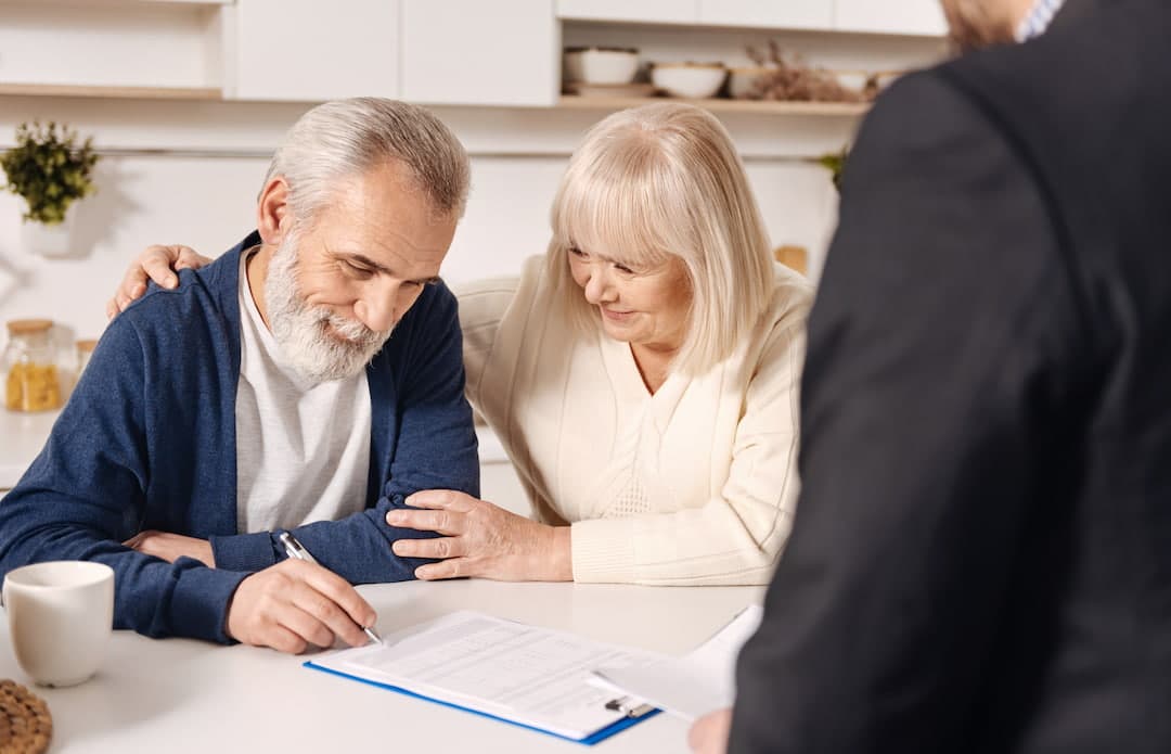 A senior couple signing documents with an agent