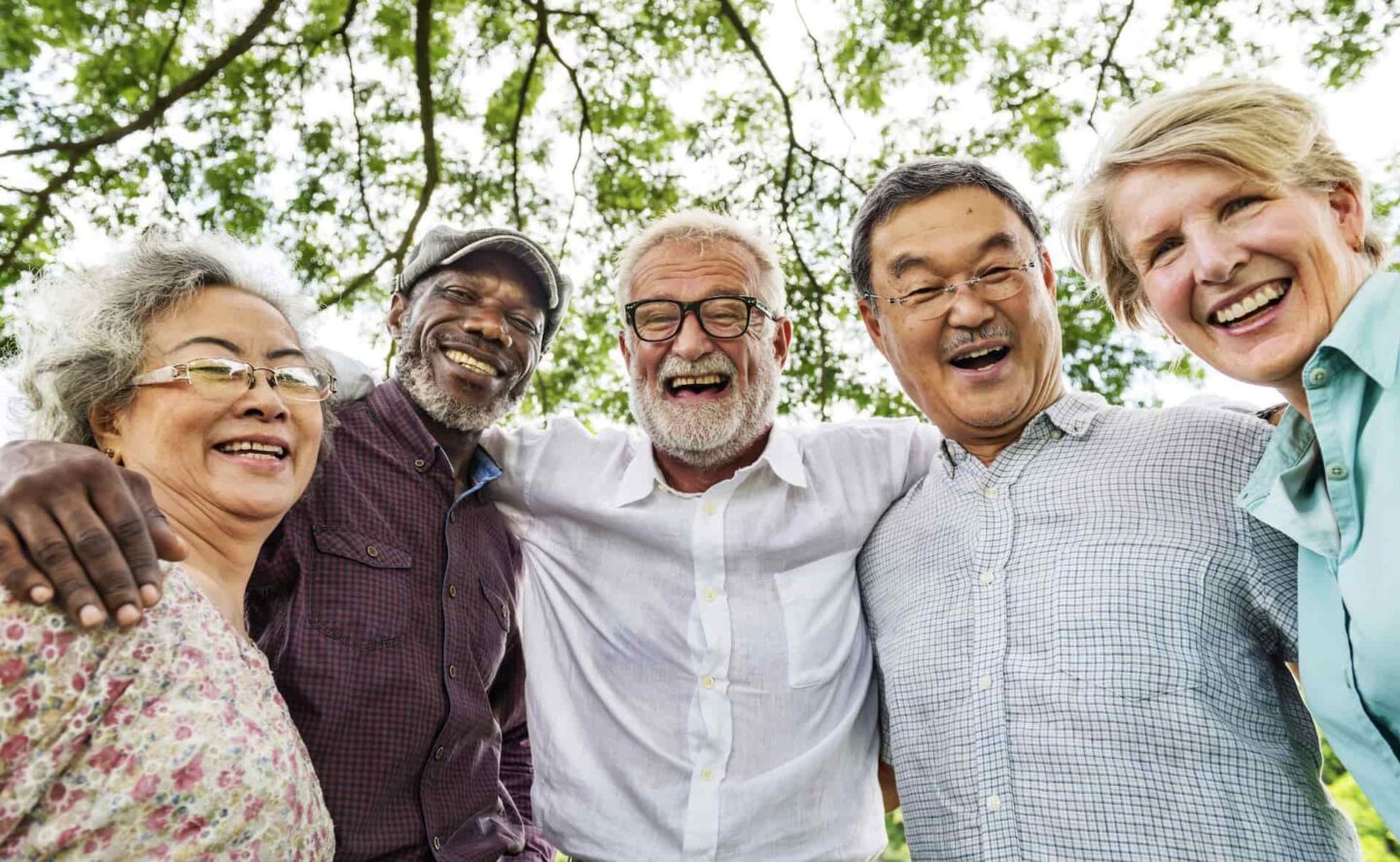 Five seniors huddled together with their arms over each others shoulders smiling in a park