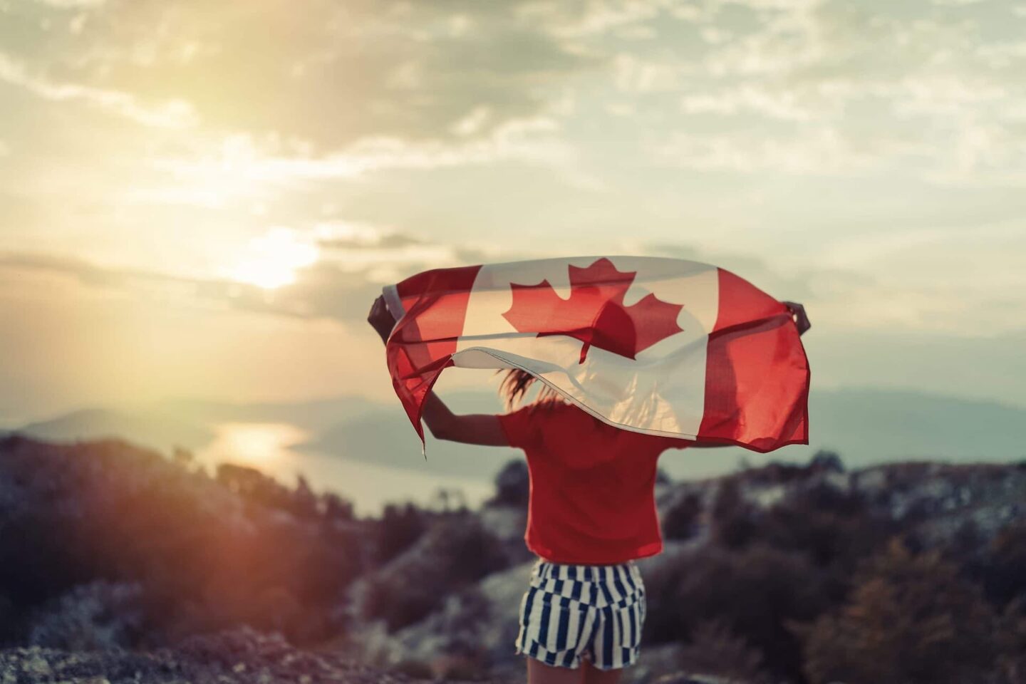 A woman holding a Canadian flag up into the wind on top of a mountain