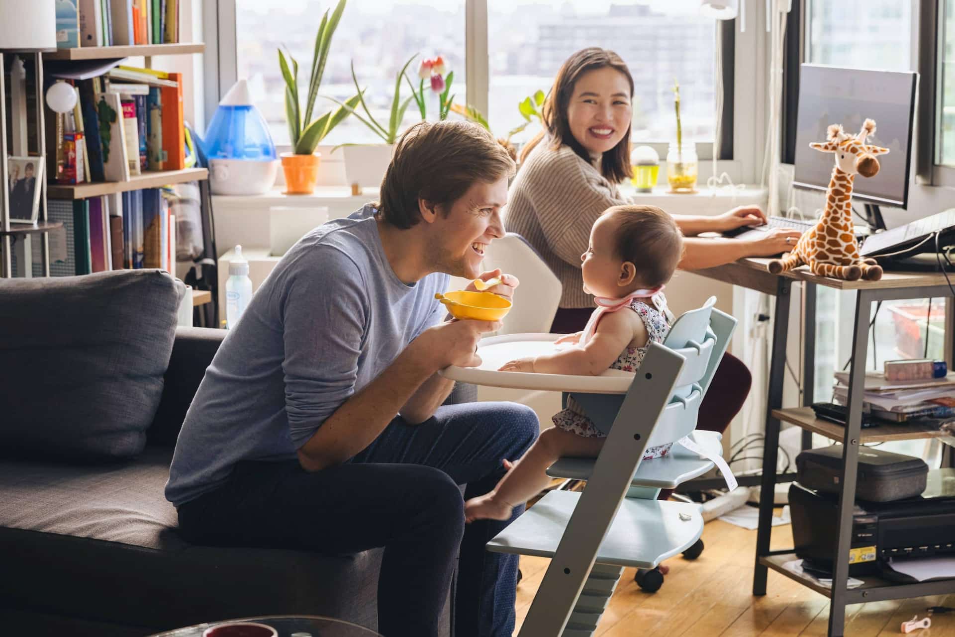 A young father laughing while feeding his infant in a highchair