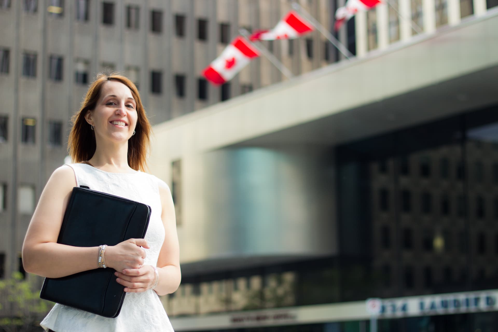 An agent standing in front of an office building that has Canadian flags hanging above the entrance