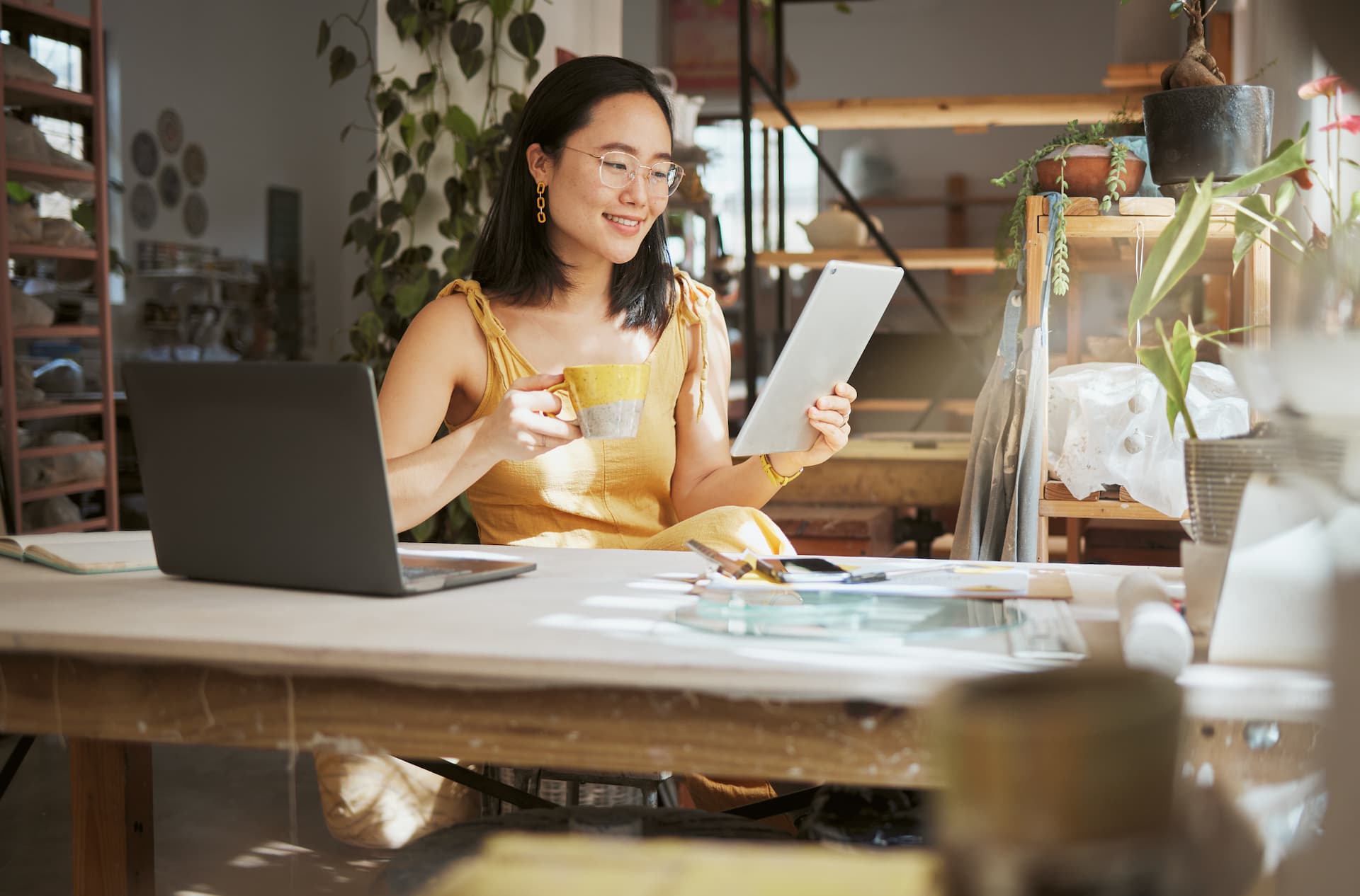 A small business owner smiling while looking at a tablet and drinking a coffee