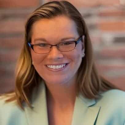 Professional woman smiling, wearing glasses, in a business setting.