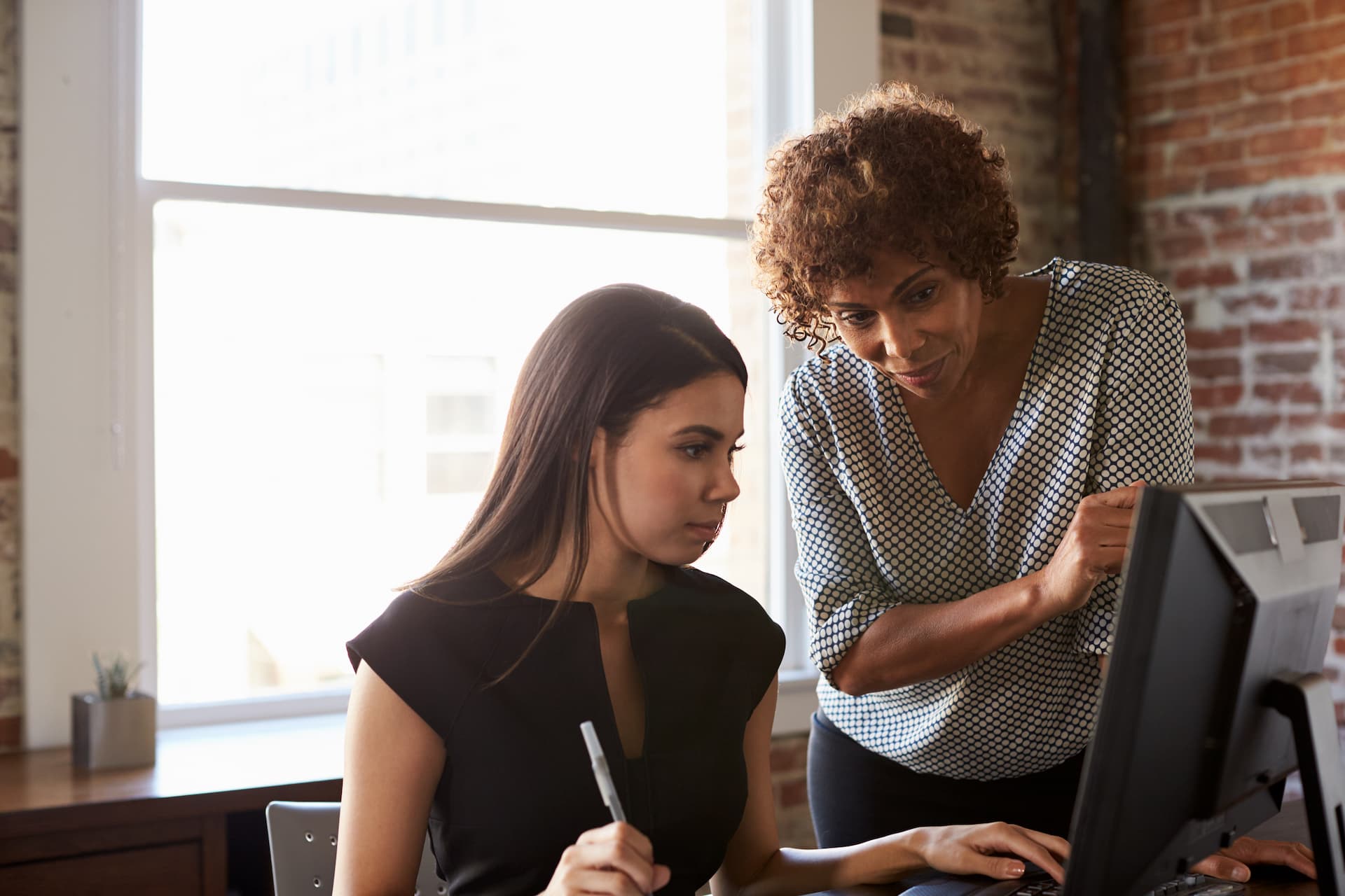 An experienced insurance agent guiding a younger agent through a task on a computer