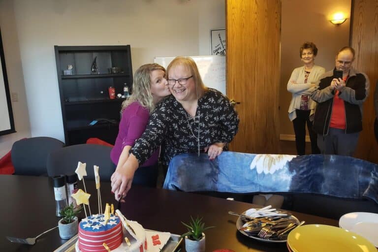 Rochelle Barber smiling while cutting a celebration cake at Experior Financial office during her retirement gathering surrounded by colleagues.